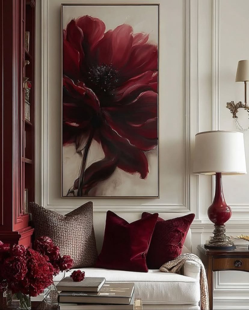 Vertical floral canvas above an ivory sofa with velvet cushions, a garnet lamp and a lacquered red bookcase
