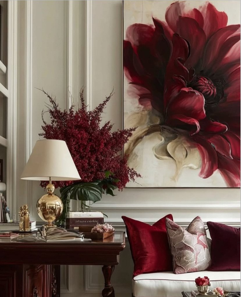 Ivory panelled salon with a large bordeaux floral painting, a brass lamp, red berries and velvet cushions